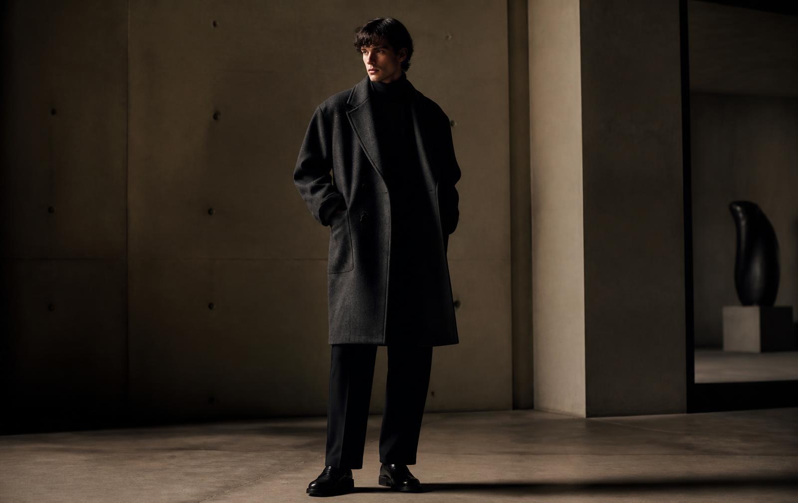 Model in an oversized charcoal wool coat inside a concrete gallery